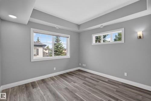 Spacious room featuring wood-finish flooring, two windows, recessed lighting, a wall sconce, and tray ceiling detailing - 18 2565 Hanna Crescent, Edmonton, AB 