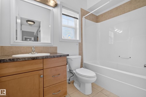 Bathroom featuring a wood-finish vanity with a built-in sink, a framed mirror, and an overhead light fixture - 18 2565 Hanna Crescent, Edmonton, AB 