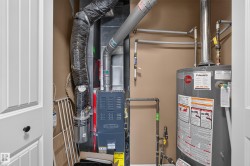 Utility closet featuring a water heater and furnace with exposed ductwork and piping - 