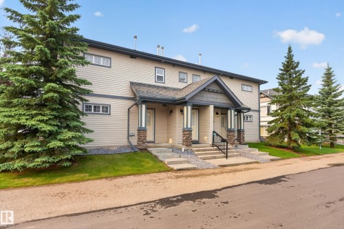 Duplex exterior featuring light-toned siding with dark trim, a covered entry with stone-wrapped columns, and multiple windows - 18 2565 Hanna Crescent, Edmonton, AB 