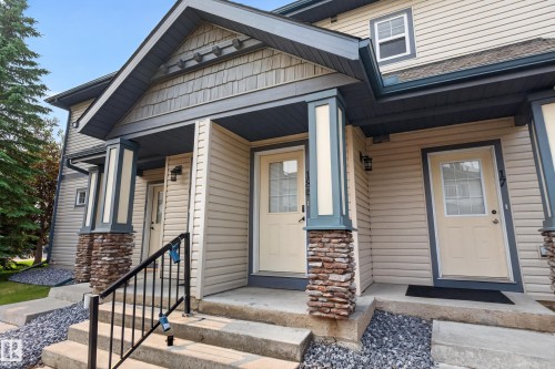 Multi-unit exterior featuring light-colored horizontal siding, a covered entry with dark trim, and stone-wrapped pillars - 18 2565 Hanna Crescent, Edmonton, AB 