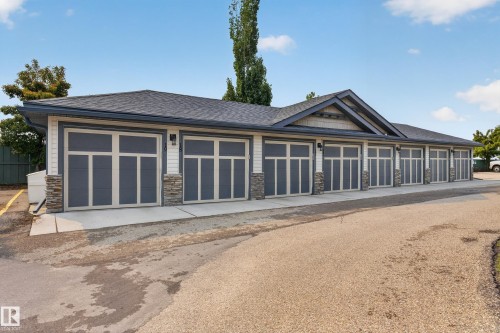 Multi-unit garage structure featuring a gabled roofline, stone accent columns, white siding, and several dark gray garage doors with light-colored trim - 18 2565 Hanna Crescent, Edmonton, AB 