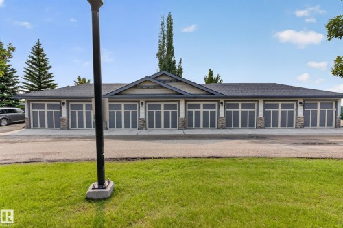 Multi-unit structure featuring eight garage doors with frosted glass panels, light siding, and stone veneer accents - 18 2565 Hanna Crescent, Edmonton, AB 