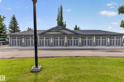 Multi-unit structure featuring eight garage doors with frosted glass panels, light siding, and stone veneer accents - 
