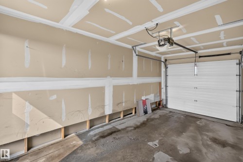 Attached garage with exposed drywall, concrete flooring, and a sectional overhead door - 18 2565 Hanna Crescent, Edmonton, AB 