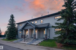 Duplex exterior featuring light-colored siding, a covered entry with stone-wrapped columns, and a dark shingle roof - 