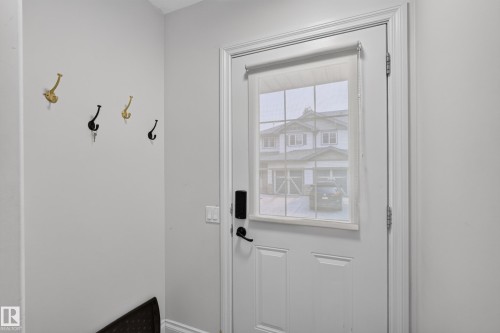 Entryway featuring a white paneled door with integrated window and privacy blind, smart lock hardware, and light gray wall paint - 18 2565 Hanna Crescent, Edmonton, AB 