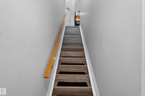 Staircase featuring wood-finish treads with dark risers, a light wood handrail, and white painted walls - 18 2565 Hanna Crescent, Edmonton, AB 