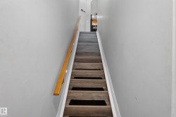 Staircase featuring wood-finish treads with dark risers, a light wood handrail, and white painted walls - 