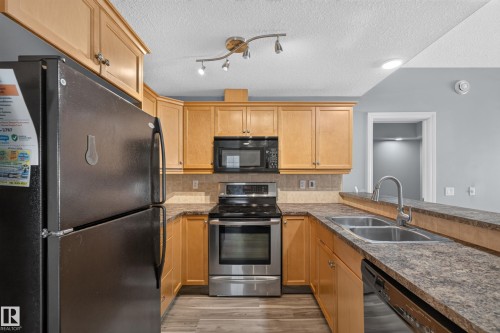 Kitchen featuring wood-finish cabinetry, stainless steel appliances, a double basin sink, and a breakfast bar - 18 2565 Hanna Crescent, Edmonton, AB 