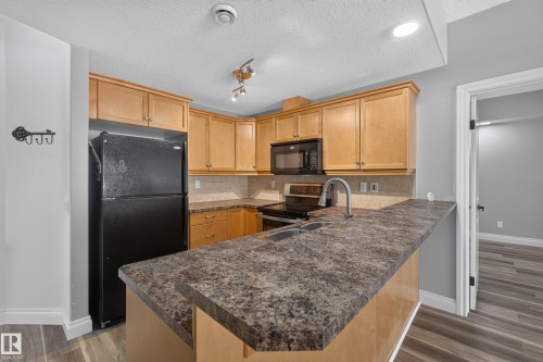Kitchen featuring wood cabinetry, black appliances, a double basin sink, and wood-finish flooring - 18 2565 Hanna Crescent, Edmonton, AB 