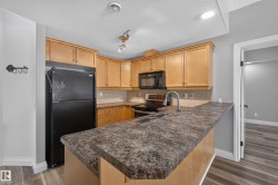 Kitchen featuring wood cabinetry, black appliances, a double basin sink, and wood-finish flooring - 