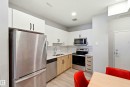 Modern kitchen featuring stainless steel appliances, white upper cabinetry, light wood-finish lower cabinetry, a subway tile backsplash, and light-toned countertops - 106 856 Secord Boulevard Nw, Edmonton, AB 