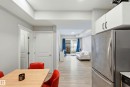 Open concept living space featuring wood-finish flooring, white cabinetry with matte black hardware, stainless steel refrigerator, and recessed lighting - 106 856 Secord Boulevard Nw, Edmonton, AB 