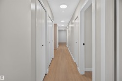 Hallway featuring wood-finish flooring, recessed lighting, white walls, and multiple white panel doors with black hardware - 