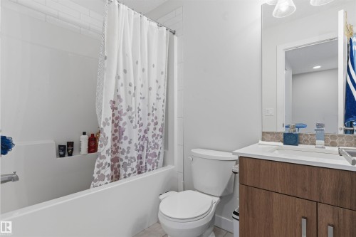 Bathroom featuring a white subway tile shower surround, a built-in tub with shelf, a floating wood-finish vanity with an undermount sink, and a hexagonal tile backsplash - 170 804 Welsh Drive, Edmonton, AB 