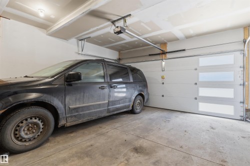Two-car garage featuring a modern sectional garage door with frosted glass panels, concrete flooring, and an exposed ceiling - 170 804 Welsh Drive, Edmonton, AB 