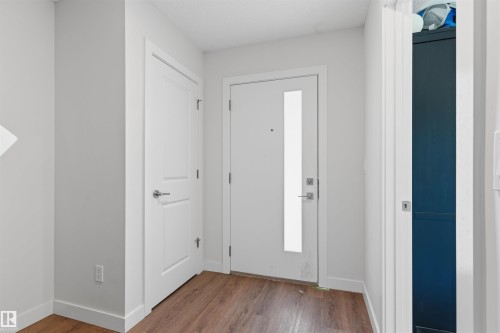Entryway featuring wood-finish flooring, a white paneled door with brushed nickel hardware, and a main entry door with a vertical frosted glass insert - 170 804 Welsh Drive, Edmonton, AB 