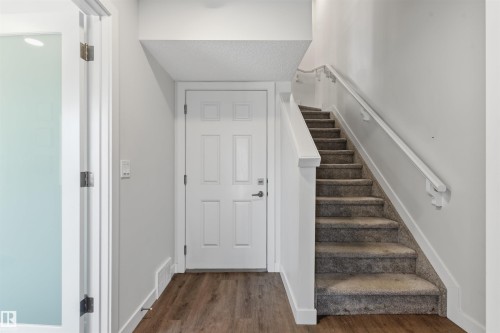Entryway featuring wood-finish flooring, a paneled door, and a staircase with carpeted treads and a white handrail - 170 804 Welsh Drive, Edmonton, AB 