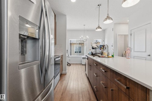 Kitchen featuring stainless steel appliances, wood-finish flooring, a long island with a light-toned countertop, and pendant lighting - 170 804 Welsh Drive, Edmonton, AB 