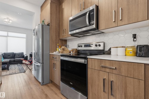 Modern kitchen featuring wood-finish cabinetry, stainless steel appliances, white hexagon tile backsplash, and light-toned countertops - 170 804 Welsh Drive, Edmonton, AB 
