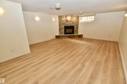 Spacious room featuring wood-finish flooring and a stone-clad fireplace - 