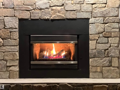 Stone-clad fireplace with a modern black inset firebox and a light-colored hearth - 7923 94 Avenue Nw, Edmonton, AB 