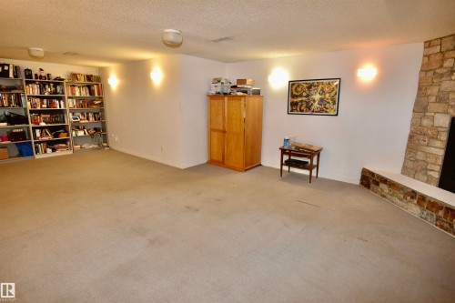 Expansive room featuring a stone fireplace with a raised hearth, wall-mounted sconces, and light-colored carpeting - 7923 94 Avenue Nw, Edmonton, AB 
