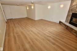 Spacious room featuring wood-finish flooring, a stone-clad fireplace with a white hearth, and recessed wall sconces - 