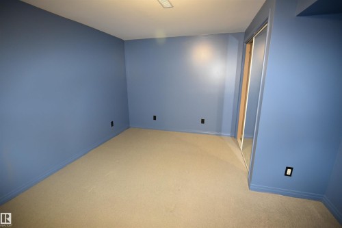 Room featuring soft blue walls, light-colored carpeting, white trim, and a mirrored sliding closet door in lower level. - 7923 94 Avenue Nw, Edmonton, AB 