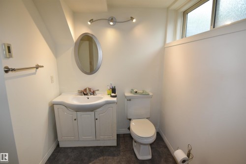 Bathroom featuring a vanity with integrated sink, oval mirror, track lighting, toilet, and a transom window in lower level - 7923 94 Avenue Nw, Edmonton, AB 