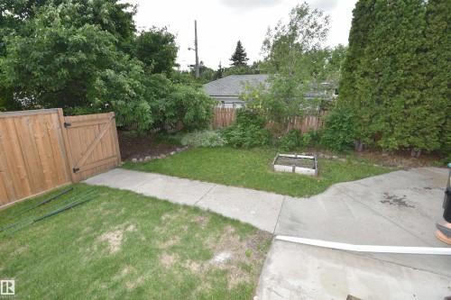 Spacious backyard with a concrete patio, grassy areas, and a wood privacy fence - 7923 94 Avenue Nw, Edmonton, AB 