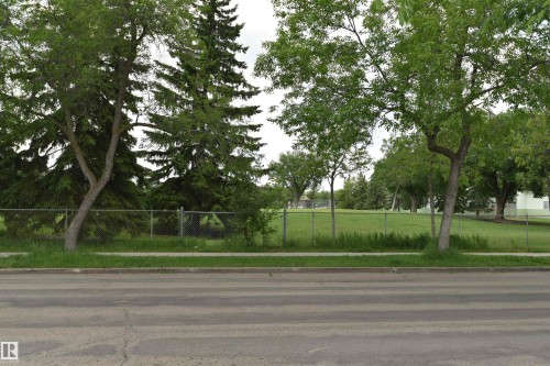 Expansive green space featuring a chain-link fence, mature trees, and a paved sidewalk along a street - 7923 94 Avenue Nw, Edmonton, AB 
