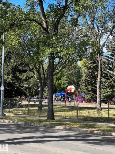 Adjacent community park featuring a basketball hoop, playground equipment, and mature trees - 7923 94 Avenue Nw, Edmonton, AB 