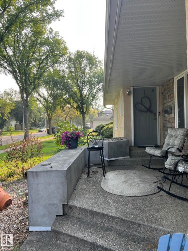 Front porch featuring a textured concrete surface and stairs, complemented by a stone accent wall - 7923 94 Avenue Nw, Edmonton, AB 