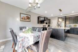 Open-concept dining and kitchen space featuring wood-finish flooring, a contemporary chandelier, recessed lighting, dark cabinetry, and a central island with a countertop - 