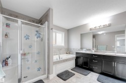 Spacious bathroom featuring a glass-enclosed shower stall with a tile surround, a built-in soaking tub with a tiled deck, a dual vanity with dark wood-finish cabinetry, and light-colored countertops - 