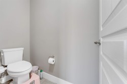 White toilet fixture with a satin nickel toilet paper holder, light gray wall paint, and white baseboards - 