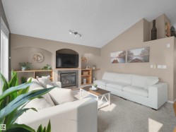 Living area featuring a vaulted ceiling, built-in shelving, a fireplace with a stone surround, and carpet flooring - 