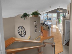 Open-concept living space featuring vaulted ceilings, wood-finish flooring, a kitchen island with sink, and a full wall of windows - 