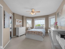 Carpeted bedroom featuring a ceiling fan, bay windows, and a doorway opening to an additional room - 