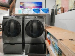 Dedicated laundry area featuring two front-loading machines with pedestals, a built-in wood-finish countertop, and overhead shelving - 