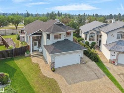 Two-story residence featuring a two-car garage, stone accents, light grey siding, a dark shingle roof, and a concrete driveway - 