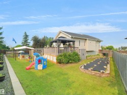 Expansive backyard featuring a large elevated wood deck with a gazebo, a raised garden bed with stone block edging, a manicured lawn, and a privacy fence - 