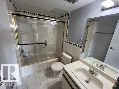Full bathroom featuring a tub with glass sliding doors, a vanity with an integrated sink, and tiled flooring - 1101 10011 123 Street, Edmonton, AB 