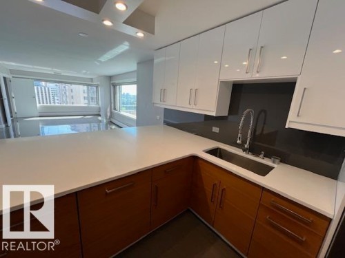 Modern kitchen featuring a large white countertop, stainless steel sink with a high arc faucet, and two-tone cabinetry with white upper and wood-finish lower cabinets - 1101 10011 123 Street, Edmonton, AB 