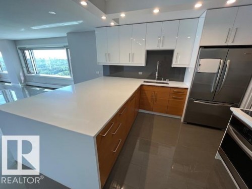 Modern kitchen featuring a large white countertop island, white upper cabinetry, and wood-finish lower cabinetry - 1101 10011 123 Street, Edmonton, AB 