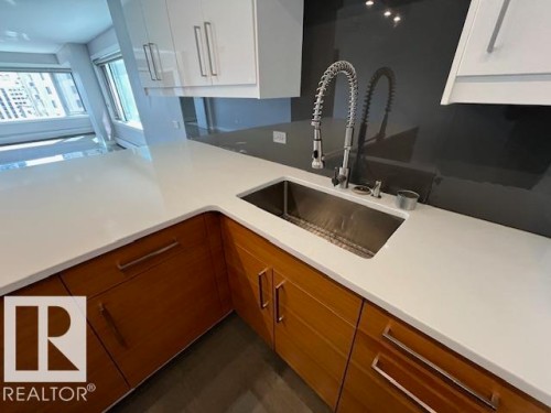 Contemporary kitchen featuring white solid surface countertops and a large undermount stainless steel sink with a professional-style pull-down faucet - 1101 10011 123 Street, Edmonton, AB 