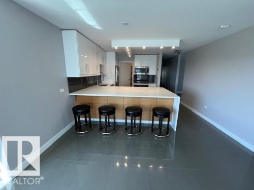 Modern kitchen featuring an expansive island with a light-toned countertop and wood-finish cabinetry - 1101 10011 123 Street, Edmonton, AB 