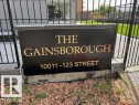 Black and gold building signage for "The Gainsborough" and address "10011 - 123 Street," framed by black metal fencing, a paver walkway, and manicured turf - 1101 10011 123 Street, Edmonton, AB 